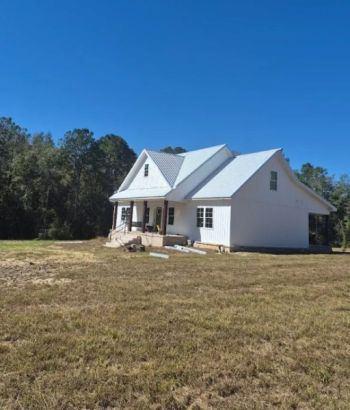 White house with newly installed metal roof on a rural property under a clear blue sky