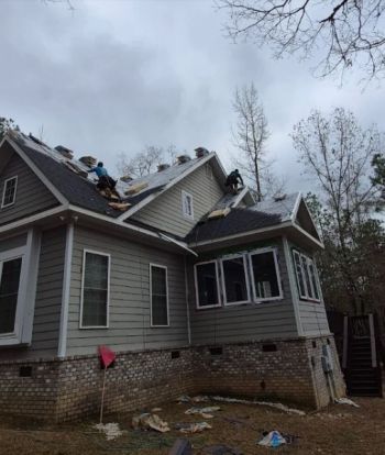 Roofing crew replacing shingles on a residential house with workers on the roof